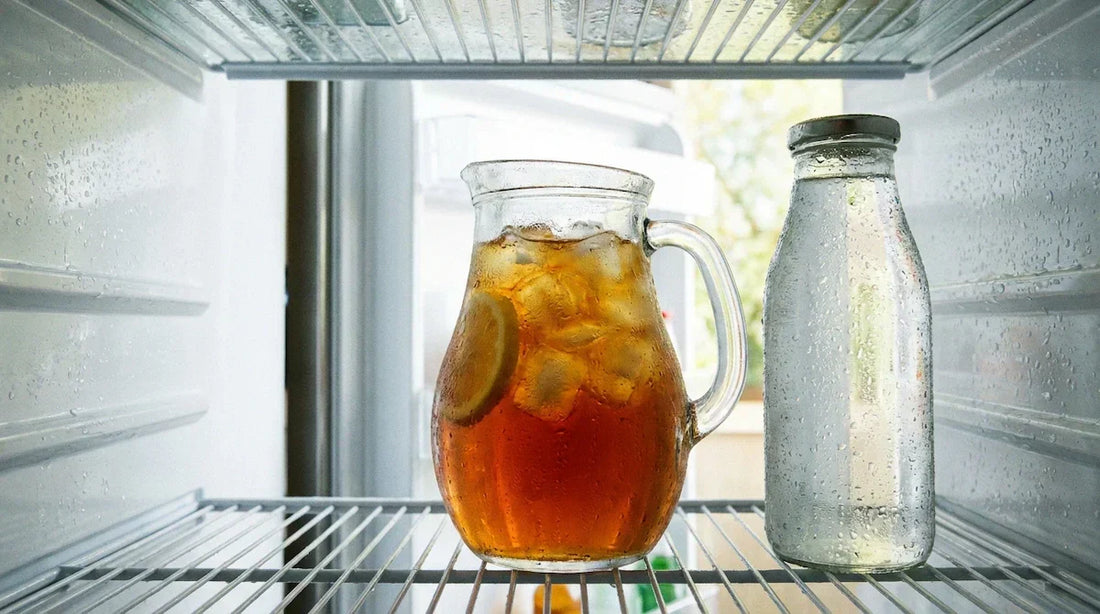 A glass pitcher of iced tea with lemon inside a bright refrigerator next to a lidded bottle.