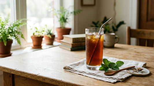 Tall glass of amber iced tea with condensation on a light oak desk, fresh mint sprigs beside it, soft natural light