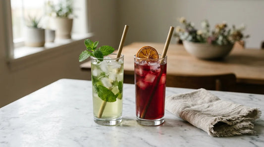 Two tall glasses on a marble surface — pale green mint iced tea beside deep ruby hibiscus citrus iced tea, both with ice and garnishes