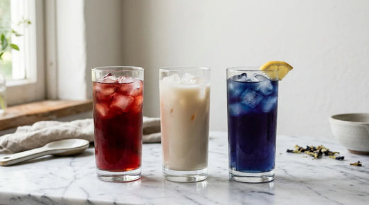 Three tall glasses of red, white, and blue layered iced tea on a marble surface for Fourth of July