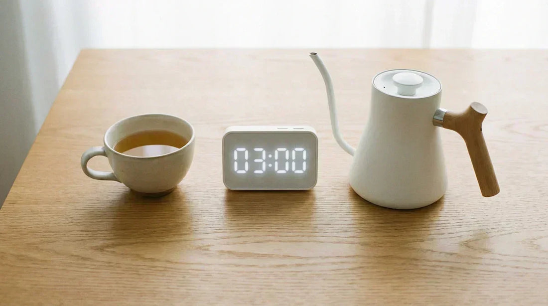 A minimalist photo of a teacup, timer, and kettle on a wooden table, illustrating the essential tools for tea brewing basics under natural light.