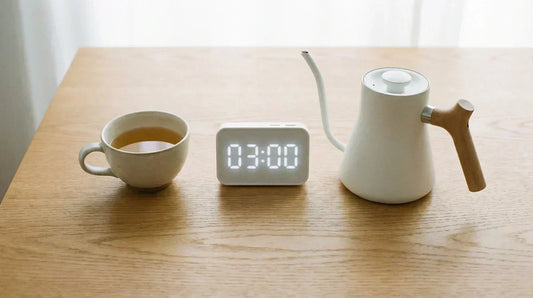 A minimalist photo of a teacup, timer, and kettle on a wooden table, illustrating the essential tools for tea brewing basics under natural light.