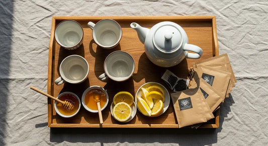 Wooden tea tray with ceramic cups, teapot, honey, lemon, and tea sachets arranged on a linen tablecloth for guests