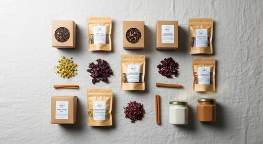Assorted tea sampler gift set with kraft boxes and resealable pouches arranged on a linen surface with dried botanicals